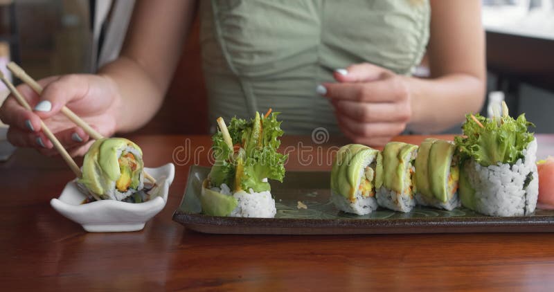 поедание суши в ресторане с палочками. женщина наслаждается обедом в ресторане ест зеленый суши. женщина ест