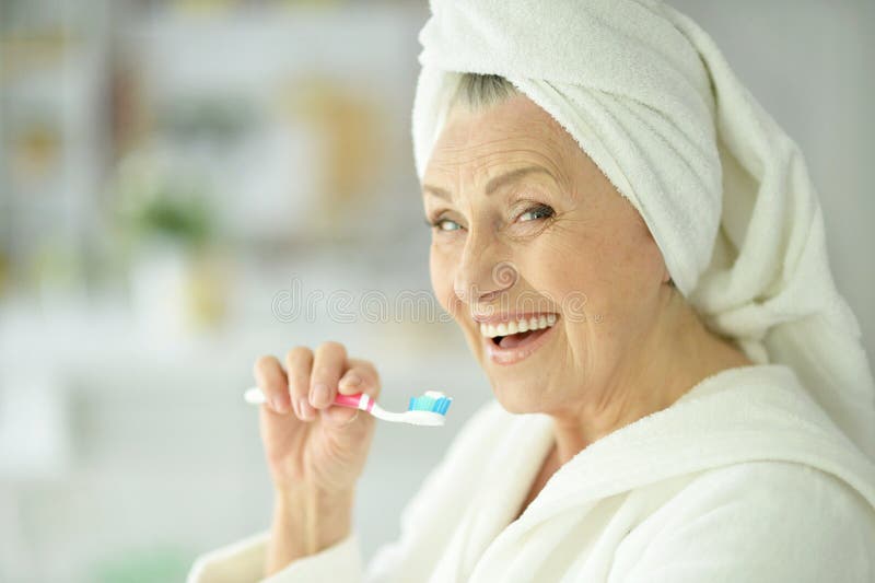 Elderly woman brushing her teeth in the bathroom. Elderly woman brushing her teeth in the bathroom