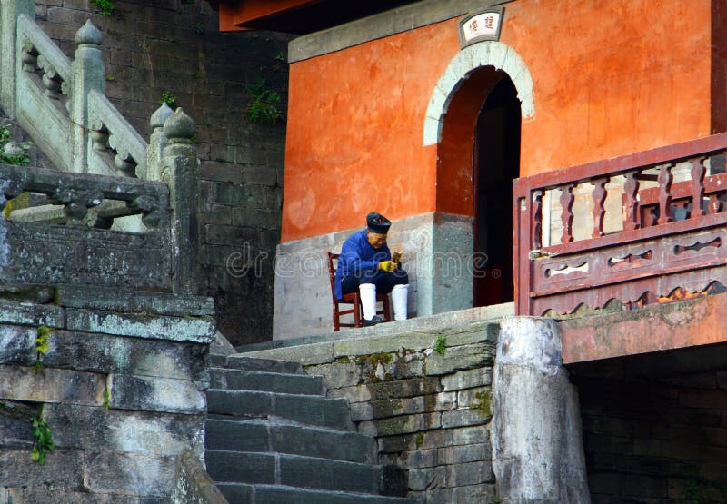 Пожилой монах taoist сидя на входе к фиолетовому виску в горах Wudang, провинции облака Хубэй стоковое изображение rf Пожилой монах taoist сидя на входе к фиолетовому виску в горах Wudang, провинции облака Хубэй стоковое изображение rf