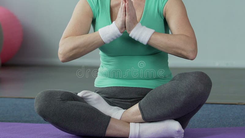 Пожилая женщина сидя на циновке йоги положив ногу на ногу, здоровье тела, внутренний баланс