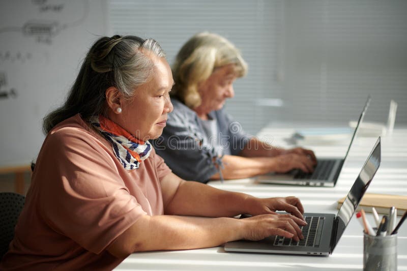 Concentrated aged woman writing e-mails on laptop as one of the task in computer class. Concentrated aged woman writing e-mails on laptop as one of the task in computer class