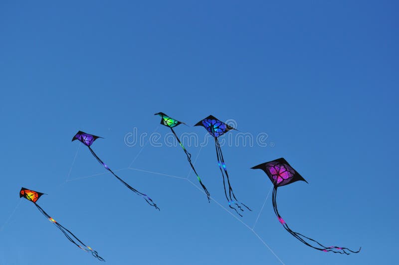 Five colored kites fly together in tandem in a cloudless blue sky. Five colored kites fly together in tandem in a cloudless blue sky