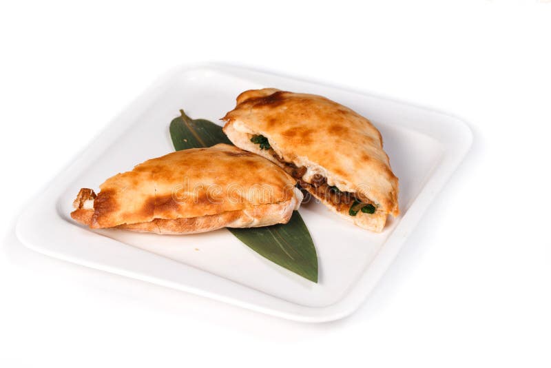 Половины пиццы Calzone на бамбуковом листе в плите на изолированной белой предпосылке стоковое изображение rf Половины пиццы Calzone на бамбуковом листе в плите на изолированной белой предпосылке стоковое изображение rf