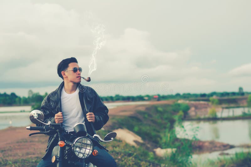 Положение человека велосипедиста курит с его мотоцилк около естественного озера и красивый, наслаждающся свободой и активным обра
