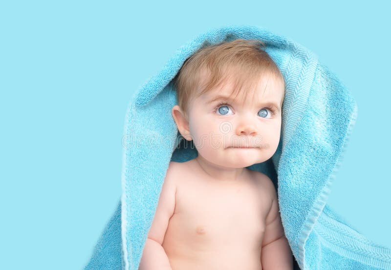 A little baby is under a blue towel and background. The child is looking up and thinking. A little baby is under a blue towel and background. The child is looking up and thinking.