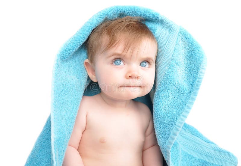 A young baby is hiding under a blue towel on a white, isolated background. The child is thinking and looking up slightly. A young baby is hiding under a blue towel on a white, isolated background. The child is thinking and looking up slightly.