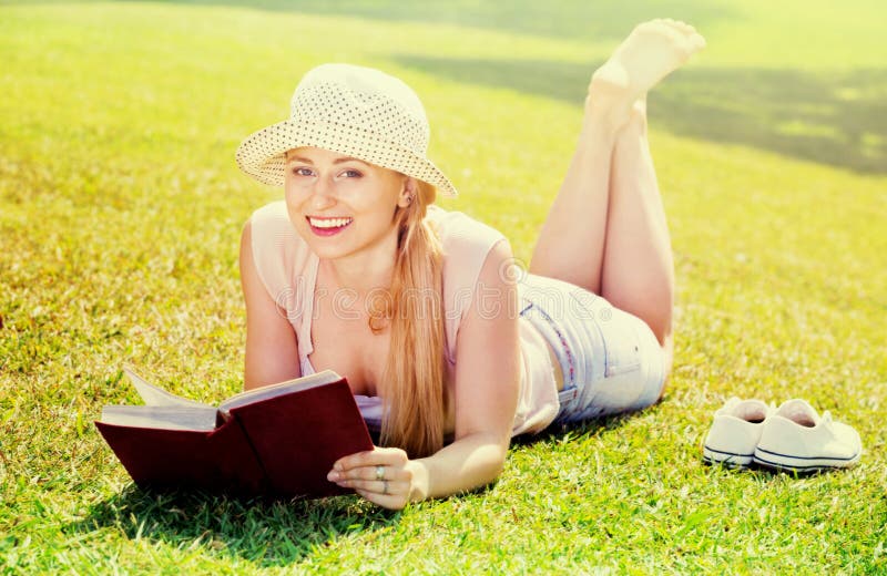 Портрет l женщины лежа на зеленой лужайке в книге парка и чтения стоковая фотография Портрет l женщины лежа на зеленой лужайке в книге парка и чтения стоковая фотография