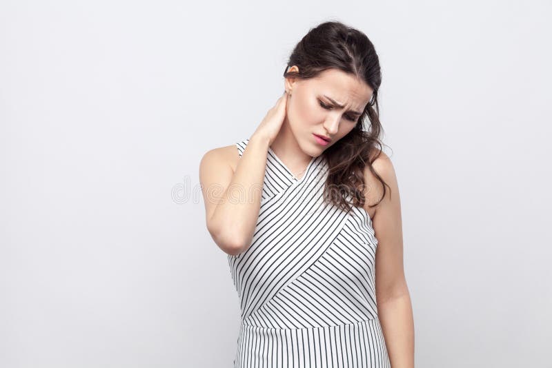 Портрет больной молодой женщины брюнета с макияжем и striped положением платья держа ее шею и чувствуя боль стоковые фотографии rf Портрет больной молодой женщины брюнета с макияжем и striped положением платья держа ее шею и чувствуя боль стоковые фотографии rf