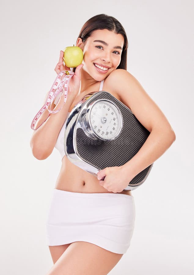 Portrait, measuring tape or happy woman with apple or scale for healthy snack, nutrition diet or digestion benefits. Smile, lose weight and fitness model with fruits in studio on white background. Portrait, measuring tape or happy woman with apple or scale for healthy snack, nutrition diet or digestion benefits. Smile, lose weight and fitness model with fruits in studio on white background.