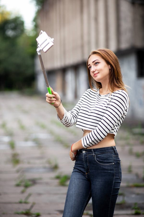 Портрет красивой девушки в городе представляя к смартфону на ручке selfie, молодой женщине делая selfie для социальной сети, конц стоковая фотография Портрет красивой девушки в городе представляя к смартфону на ручке selfie, молодой женщине делая selfie для социальной сети, конц стоковая фотография