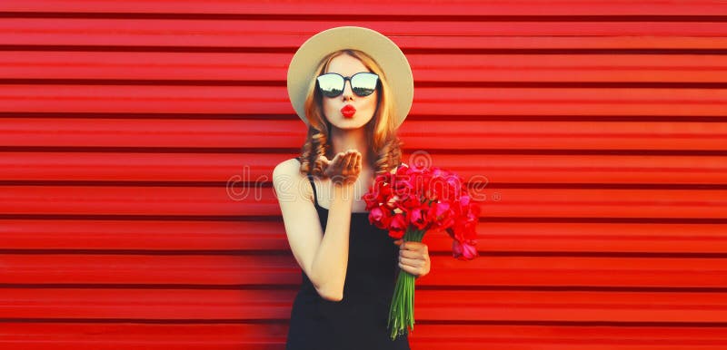 Portrait of beautiful woman with bouquet of pink flowers blowing her lips sending sweet air kiss in summer straw round hat on red background. Portrait of beautiful woman with bouquet of pink flowers blowing her lips sending sweet air kiss in summer straw round hat on red background.