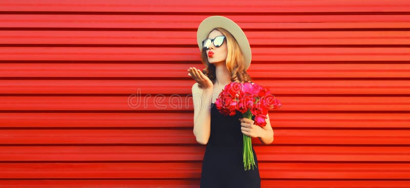 Portrait of beautiful woman with bouquet of pink flowers blowing her lips sending sweet air kiss in summer straw round hat on red background. Portrait of beautiful woman with bouquet of pink flowers blowing her lips sending sweet air kiss in summer straw round hat on red background.