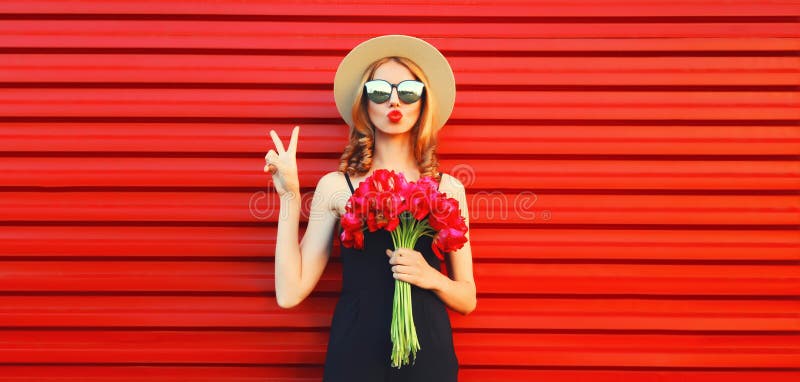 Portrait of beautiful woman with bouquet of pink flowers blowing her lips sending sweet air kiss in summer straw round hat on red background. Portrait of beautiful woman with bouquet of pink flowers blowing her lips sending sweet air kiss in summer straw round hat on red background.