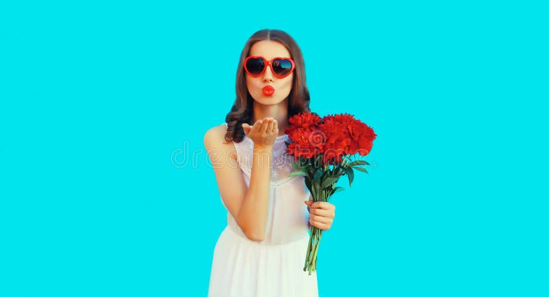 Portrait of beautiful woman with bouquet of red rose flowers and blowing her lips sending kiss in heart shaped sunglasses on blue background. Portrait of beautiful woman with bouquet of red rose flowers and blowing her lips sending kiss in heart shaped sunglasses on blue background.