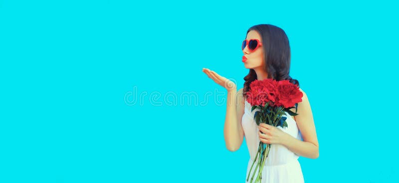 Portrait of beautiful woman with bouquet of red rose flowers and blowing her lips sending kiss in heart shaped sunglasses on blue background. Portrait of beautiful woman with bouquet of red rose flowers and blowing her lips sending kiss in heart shaped sunglasses on blue background.