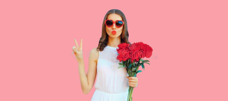 Portrait of beautiful woman with bouquet of red rose flowers and blowing her lips sending kiss in heart shaped sunglasses on pink background. Portrait of beautiful woman with bouquet of red rose flowers and blowing her lips sending kiss in heart shaped sunglasses on pink background.