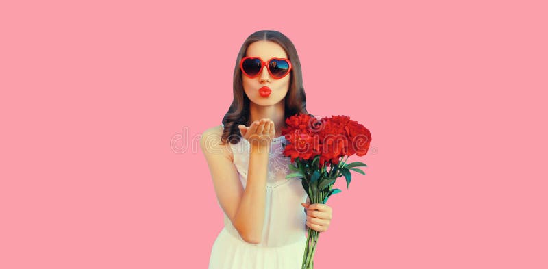 Portrait of beautiful woman with bouquet of red rose flowers and blowing her lips sending kiss in heart shaped sunglasses on pink background. Portrait of beautiful woman with bouquet of red rose flowers and blowing her lips sending kiss in heart shaped sunglasses on pink background.