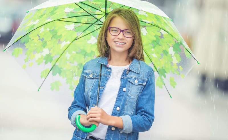 Portrait of beautiful young pre-teen girl with umbrella under spring or summer rain. Smilling girl with dental braces and glasses smile orthodontic teenage happy clear dentist boots rubber women scarf color weather walk rainy fun autumn concept happiness puddle alone street outdoor green optimism jump bad gray activity city beauty life positive blonde feminine emotions playful. Portrait of beautiful young pre-teen girl with umbrella under spring or summer rain. Smilling girl with dental braces and glasses smile orthodontic teenage happy clear dentist boots rubber women scarf color weather walk rainy fun autumn concept happiness puddle alone street outdoor green optimism jump bad gray activity city beauty life positive blonde feminine emotions playful