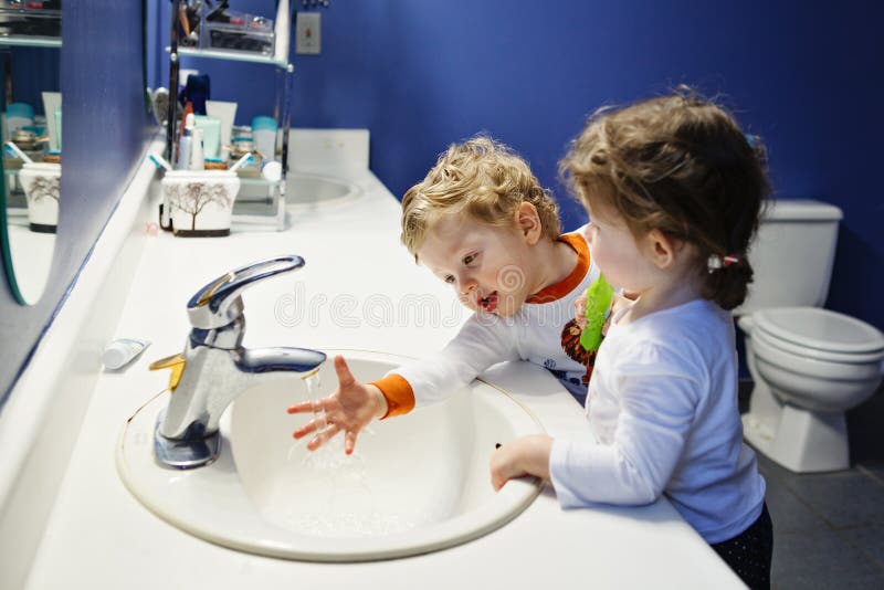 Closeup portrait of twins kids toddler boy girl in bathroom toilet washing face hands brushing teeth with toothbrash playing with water, lifestyle home style, everyday moments, morning routine. Closeup portrait of twins kids toddler boy girl in bathroom toilet washing face hands brushing teeth with toothbrash playing with water, lifestyle home style, everyday moments, morning routine