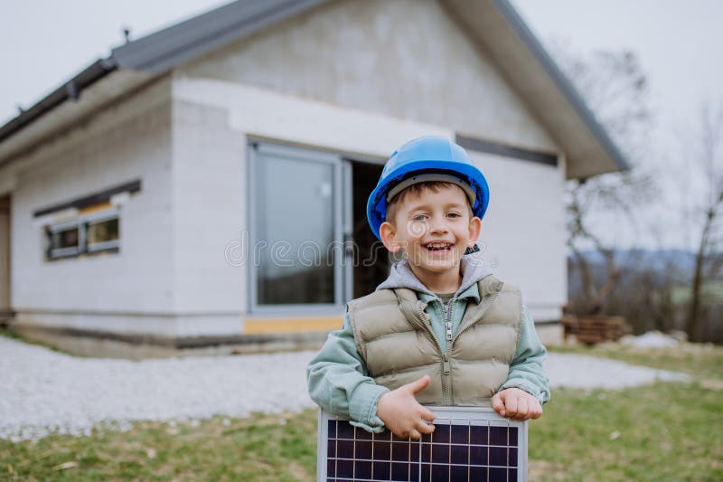 Portrait of a little boy holding solar panel, in front of their new unfinished house. Portrait of a little boy holding solar panel, in front of their new unfinished house.