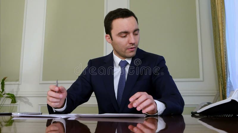 Портрет молодого бизнесмена работая на его обработке документов в офисе сток-видео Портрет молодого бизнесмена работая на его обработке документов в офисе сток-видео