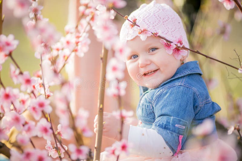 Close-up portrait of a 1-2 year old girl outdoors in a garden with pink flowers in the trees. Close-up portrait of a 1-2 year old girl outdoors in a garden with pink flowers in the trees.