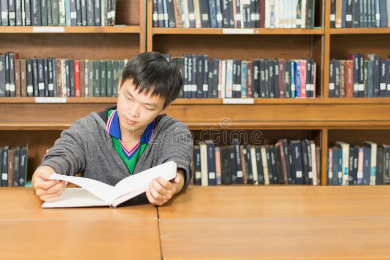 Портрет серьезного молодого студента читая книгу в библиотеке стоковые изображения rf Портрет серьезного молодого студента читая книгу в библиотеке стоковые изображения rf