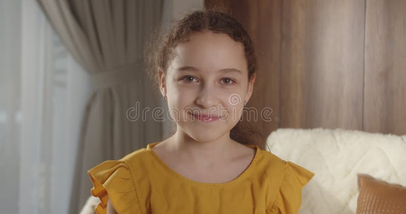 портрет смешная маленькая девочка улыбается ребенок смотрит на камеру сидит на диване дома милый ребенок с симпатичным