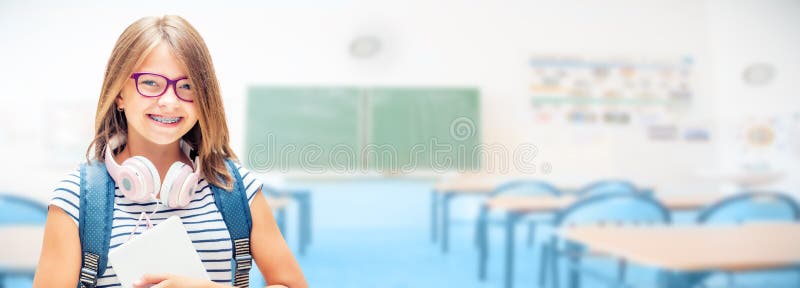 Portrait of modern happy teen school girl with bag backpackand class room as background. Girl with dental braces and glasses. Portrait of modern happy teen school girl with bag backpackand class room as background. Girl with dental braces and glasses.