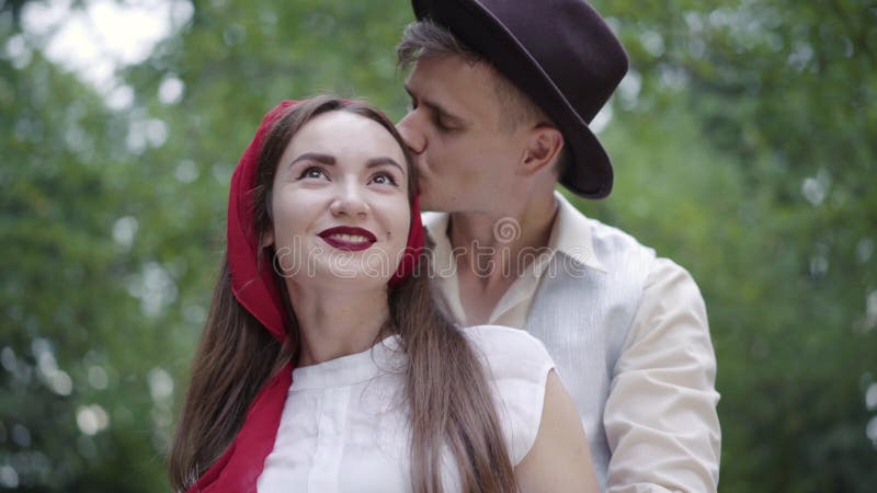 Портрет счастливого парня, целуя улыбаясь девушку на голову на открытом воздухе. Молодые любящий кавказские пары стоимостью в сток-видео