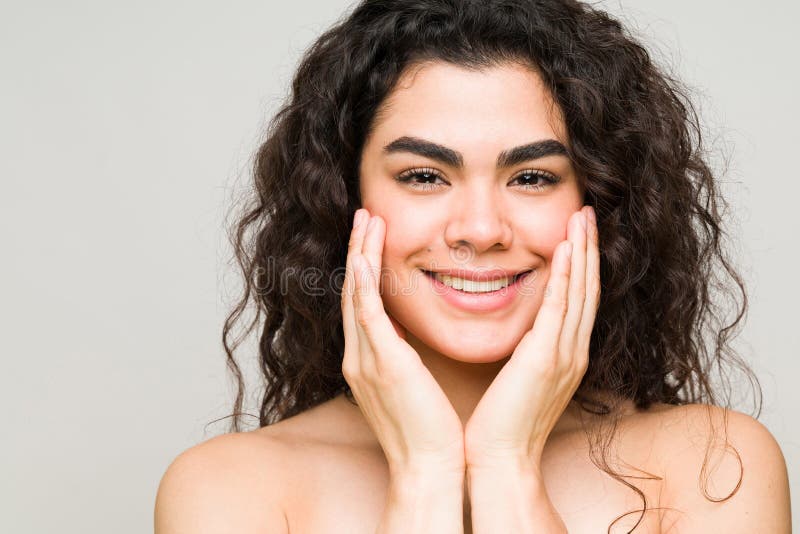 Good-looking woman with curly hair smiling and feeling her clean and fresh face after her skin care routine. Good-looking woman with curly hair smiling and feeling her clean and fresh face after her skin care routine