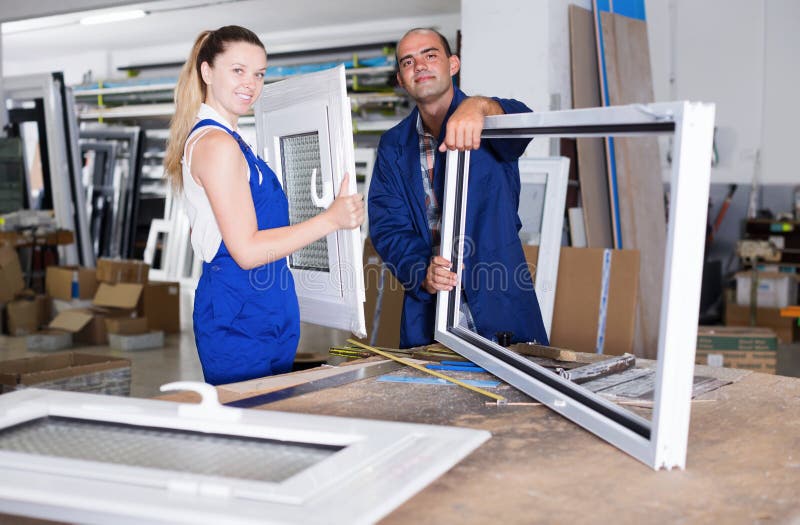 Portrait of smiling two workers in blue overalls assembling pvc windows at factory. Portrait of smiling two workers in blue overalls assembling pvc windows at factory..