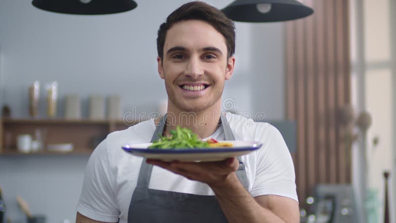 Портрет улыбаясь плиты холдинга человека с кухней шеф-повара салат дома.