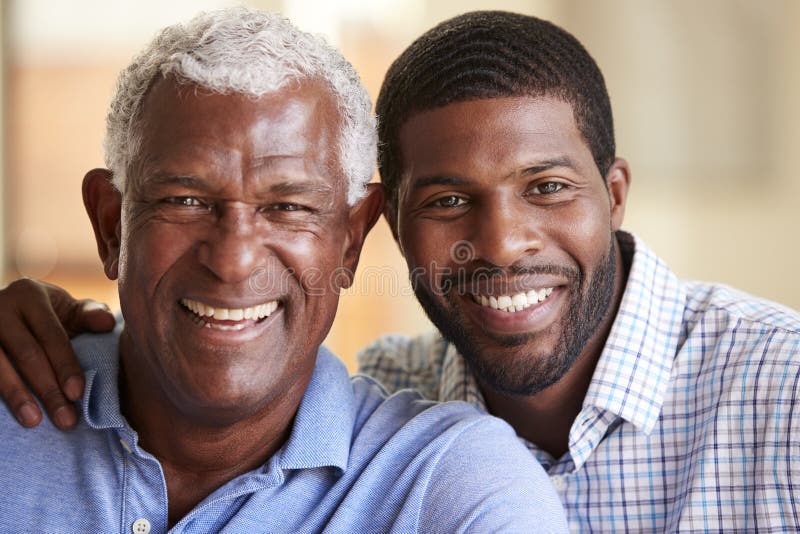 Portrait Of Smiling Senior Father Being Hugged By Adult Son At Home. Portrait Of Smiling Senior Father Being Hugged By Adult Son At Home