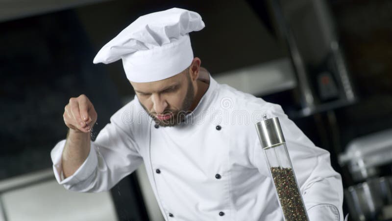 Портрет шеф-повара человека соля еду на кухне Сконцентрированный шеф-повар варя еду