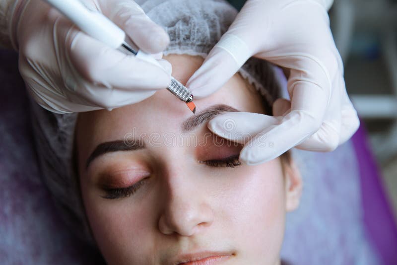Постоянный макияж для бровей Чело Microblading Beautician делая бровь татуируя для женской стороны Красивая молодая стоковая фотография Постоянный макияж для бровей Чело Microblading Beautician делая бровь татуируя для женской стороны Красивая молодая стоковая фотография