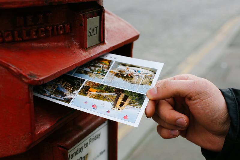 Male hand is putting a postcard in an iconic red postbox belonging to Royal Mail. Male hand is putting a postcard in an iconic red postbox belonging to Royal Mail.