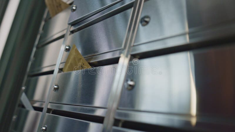 Mailman hand put letters into silver containers in hall closeup. Unrecognized worker delivering post bills inserting correspondence in building corridor. Modern metal mailbox reflecting light indoors. Mailman hand put letters into silver containers in hall closeup. Unrecognized worker delivering post bills inserting correspondence in building corridor. Modern metal mailbox reflecting light indoors.