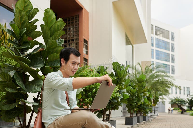 Young businessman sitting in front of office building, opening laptop to answer e-mails. Young businessman sitting in front of office building, opening laptop to answer e-mails