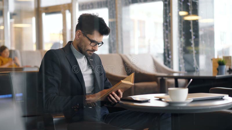 Предприниматель сфокусированный на книге чтения сидя во встрече кафа ждать