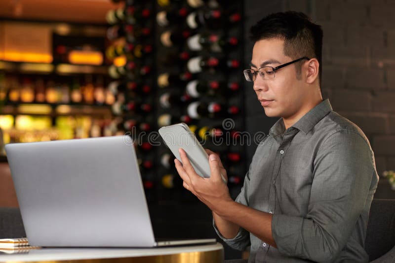 Serious young entrepreneur reading e-mails on tablet computer when working in restaurant. Serious young entrepreneur reading e-mails on tablet computer when working in restaurant