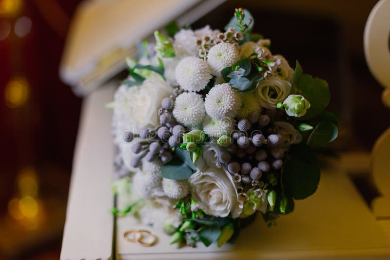 прекрасный свадебный букет золотых колец молодоженов лежит на поверхности белого пианино. день свадьбы