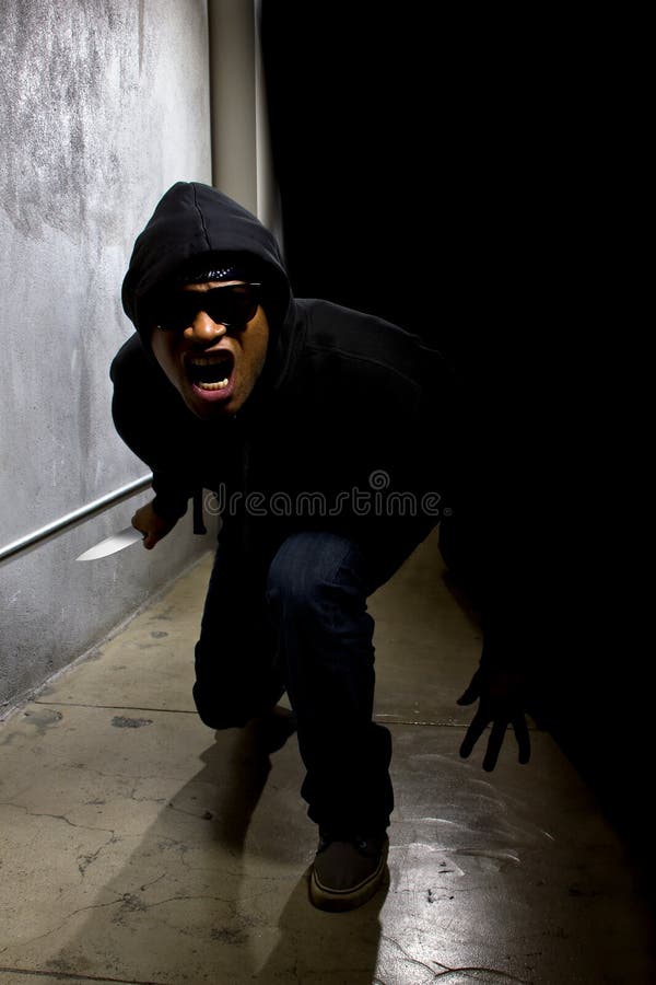 Hooded criminal with a knife hiding in the shadows of a street alley. Hooded criminal with a knife hiding in the shadows of a street alley