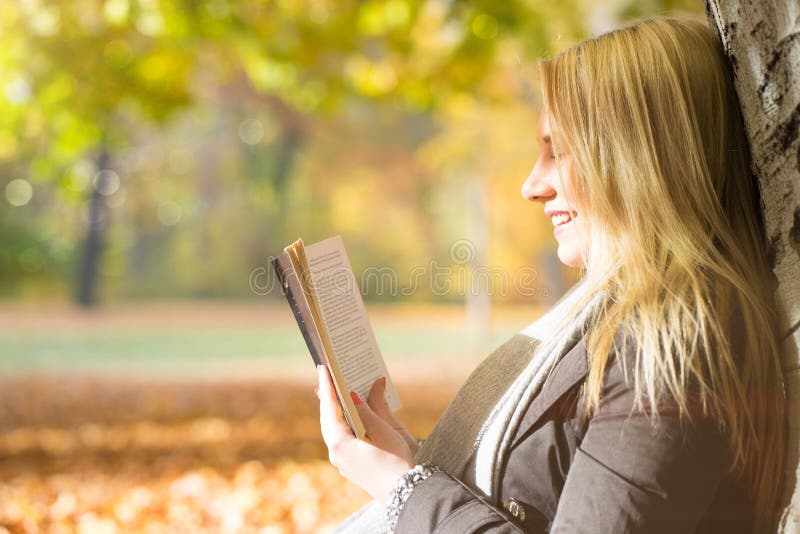 Привлекательная белокурая девушка наслаждаясь книгой в парке стоковое фото rf Привлекательная белокурая девушка наслаждаясь книгой в парке стоковое фото rf