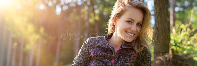 Привлекательная усмехаясь молодая белокурая женщина, нося sportswear, ослабляя после разминки в лесе стоковые фотографии rf