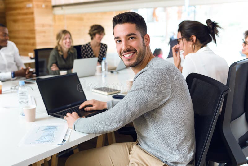 Привлекательный молодой бизнесмен работая с ноутбуком пока смотрящ камеру на coworking месте стоковое фото rf
