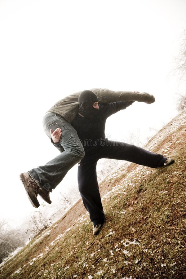 Special forces one-on-one training. Man in a black outfit and mask, lifting another man in civilian clothes onto his shoulders. Taken outdoors. Angled shot. Special forces one-on-one training. Man in a black outfit and mask, lifting another man in civilian clothes onto his shoulders. Taken outdoors. Angled shot.