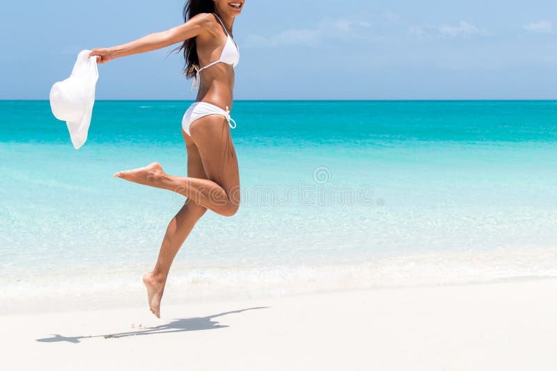 Beach ready bikini body - slim legs and toned thighs and butt. Suntan happy woman jumping in freedom on white sand with sun hat. Weight loss success or epilation concept. Beach ready bikini body - slim legs and toned thighs and butt. Suntan happy woman jumping in freedom on white sand with sun hat. Weight loss success or epilation concept.