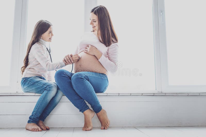 Приятная девушка слушая биение сердца ее будущего брата стоковая фотография rf