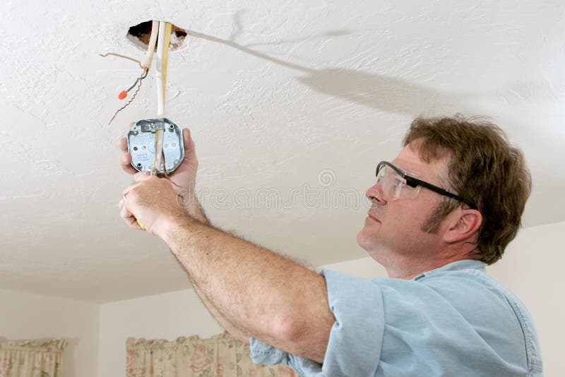 An electrician pulling wires through a ceiling fan box. Work is being performed to code by a licensed master electrician. An electrician pulling wires through a ceiling fan box. Work is being performed to code by a licensed master electrician.
